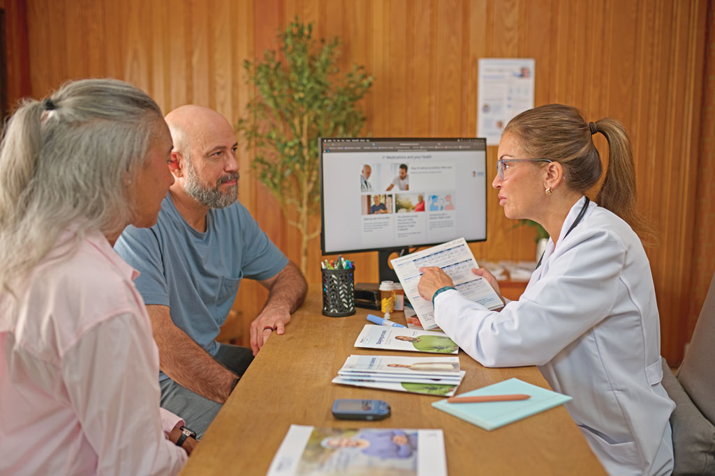 A doctor sitting at her desk across from a man and a woman and explaining a chart