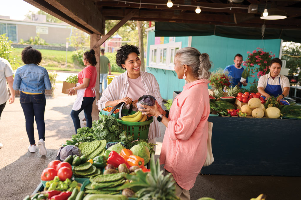 Two women putting produce in a basket at an outdoor market
